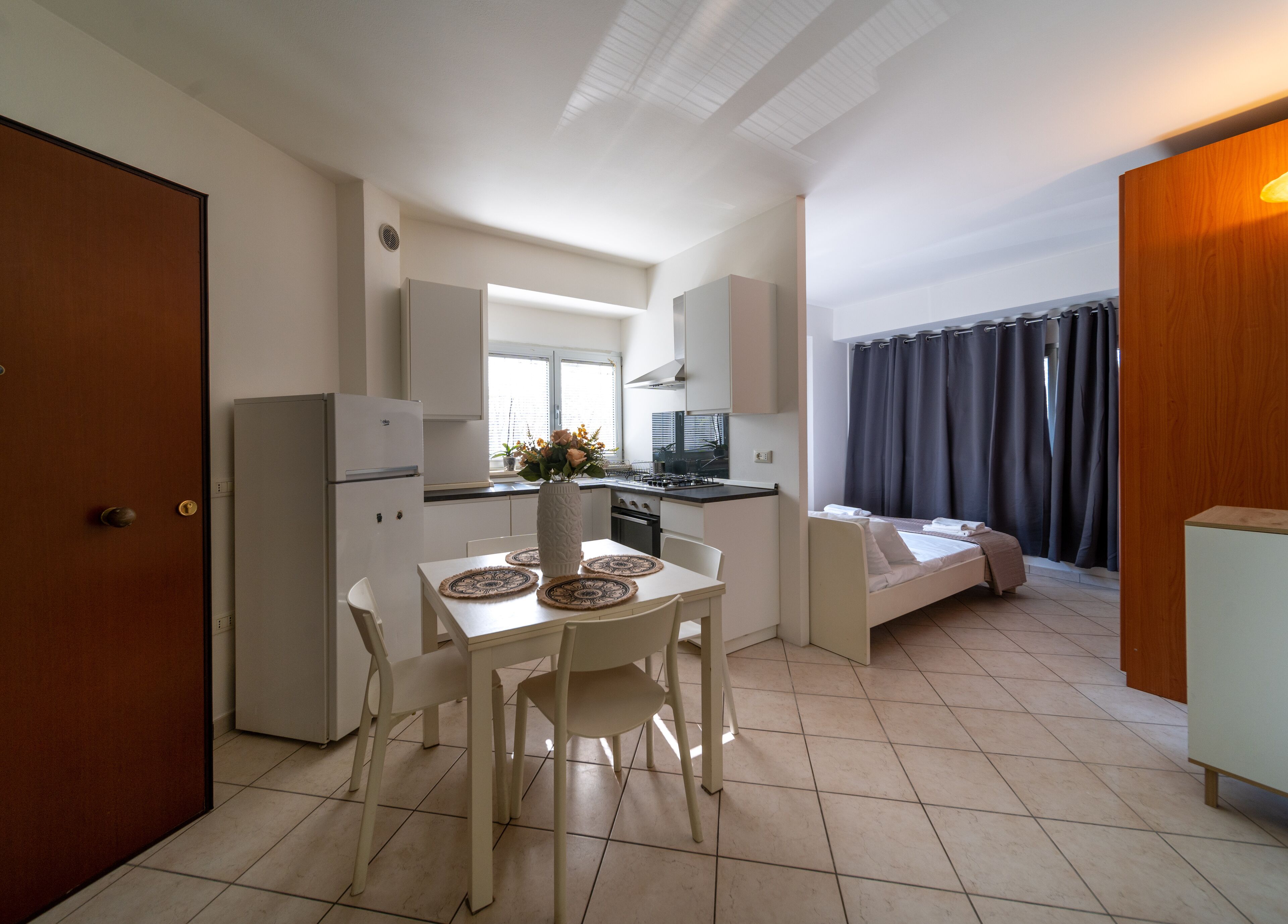 Una cocina compacta con comedor, una kitchenette y un dormitorio pequeño con cama y cortinas.