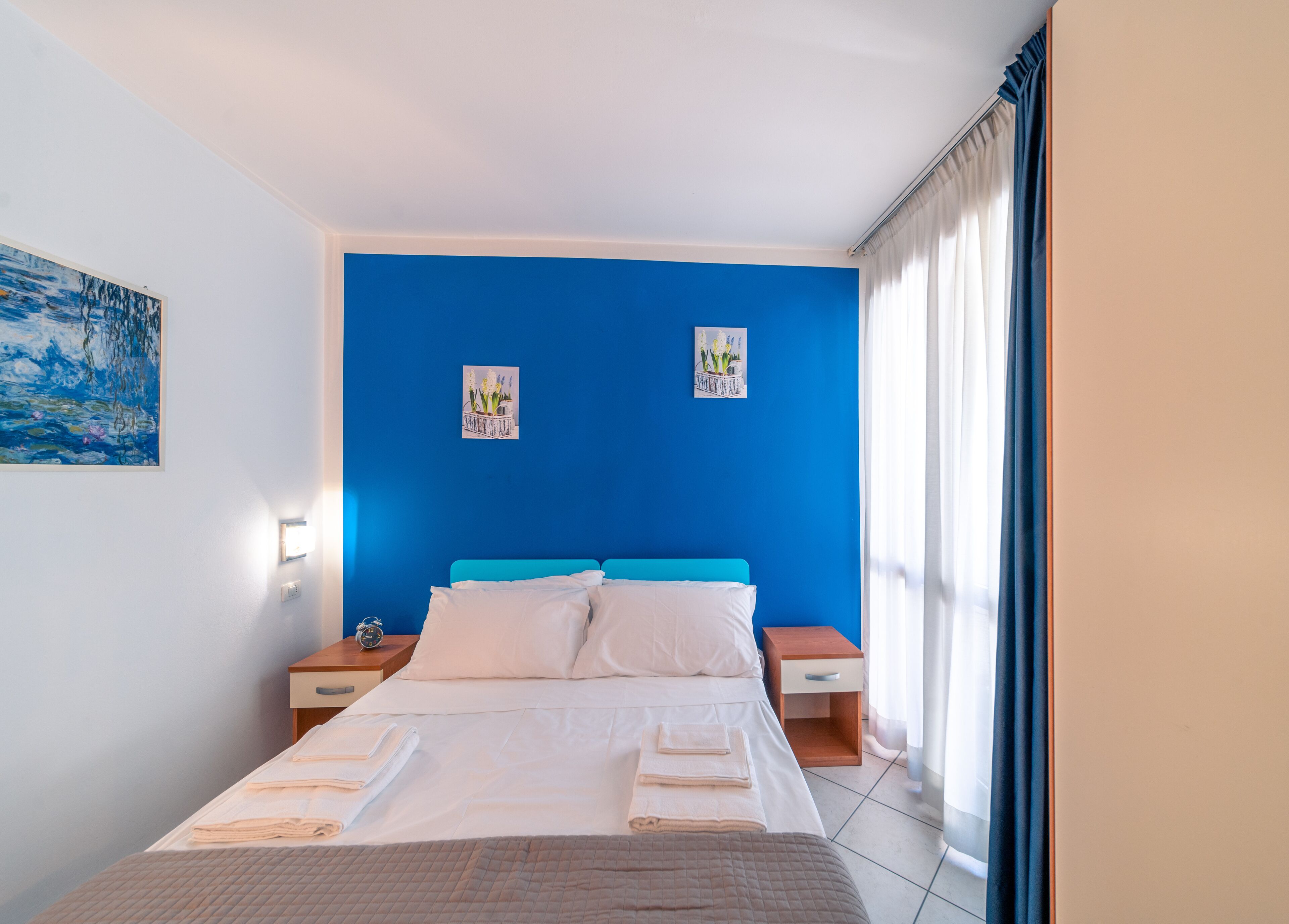 A bedroom with a blue accent wall, a bed with white linens, two bedside tables, and artwork on the wall.