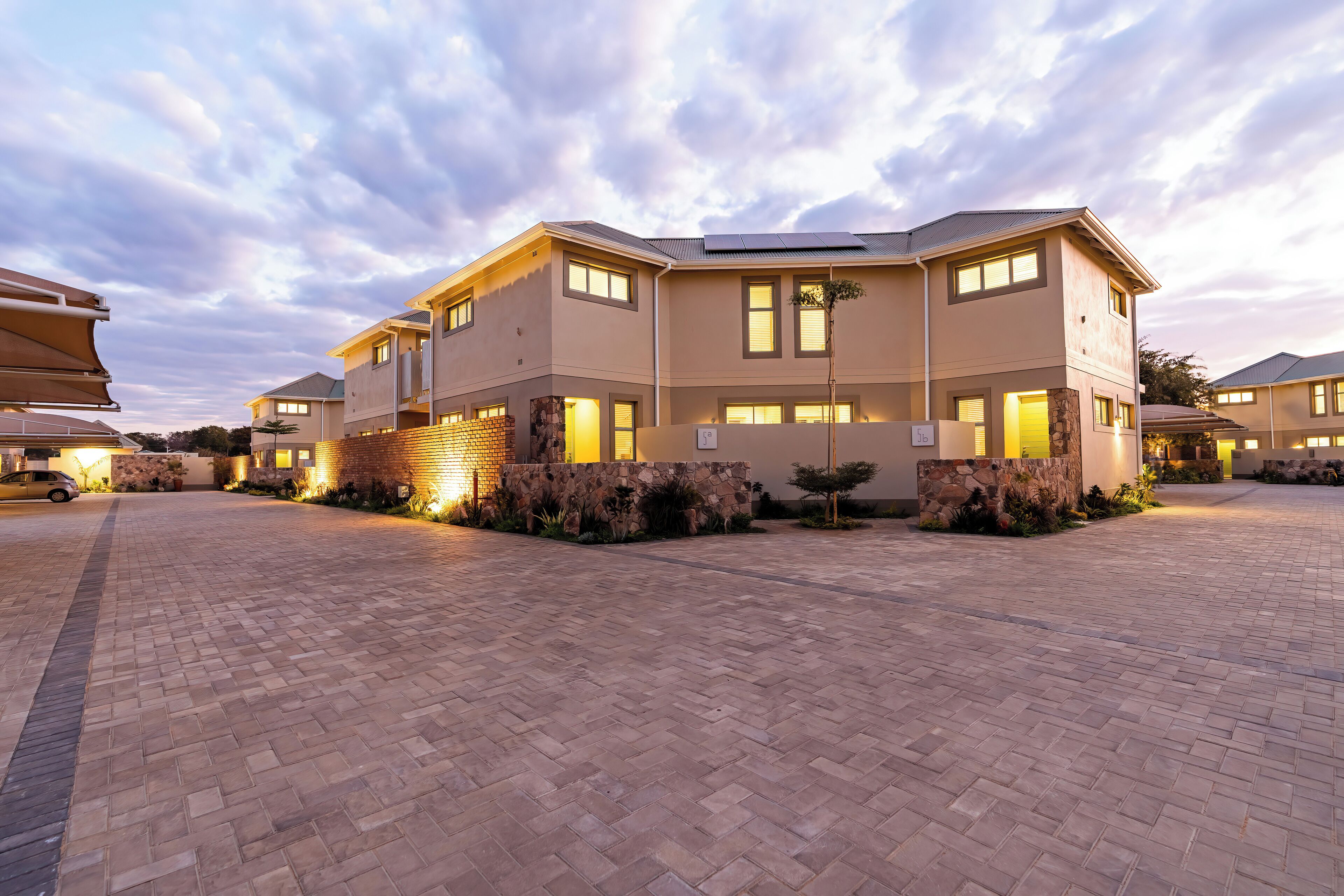 A modern multi-story residential building with a paved driveway and stone landscaping.