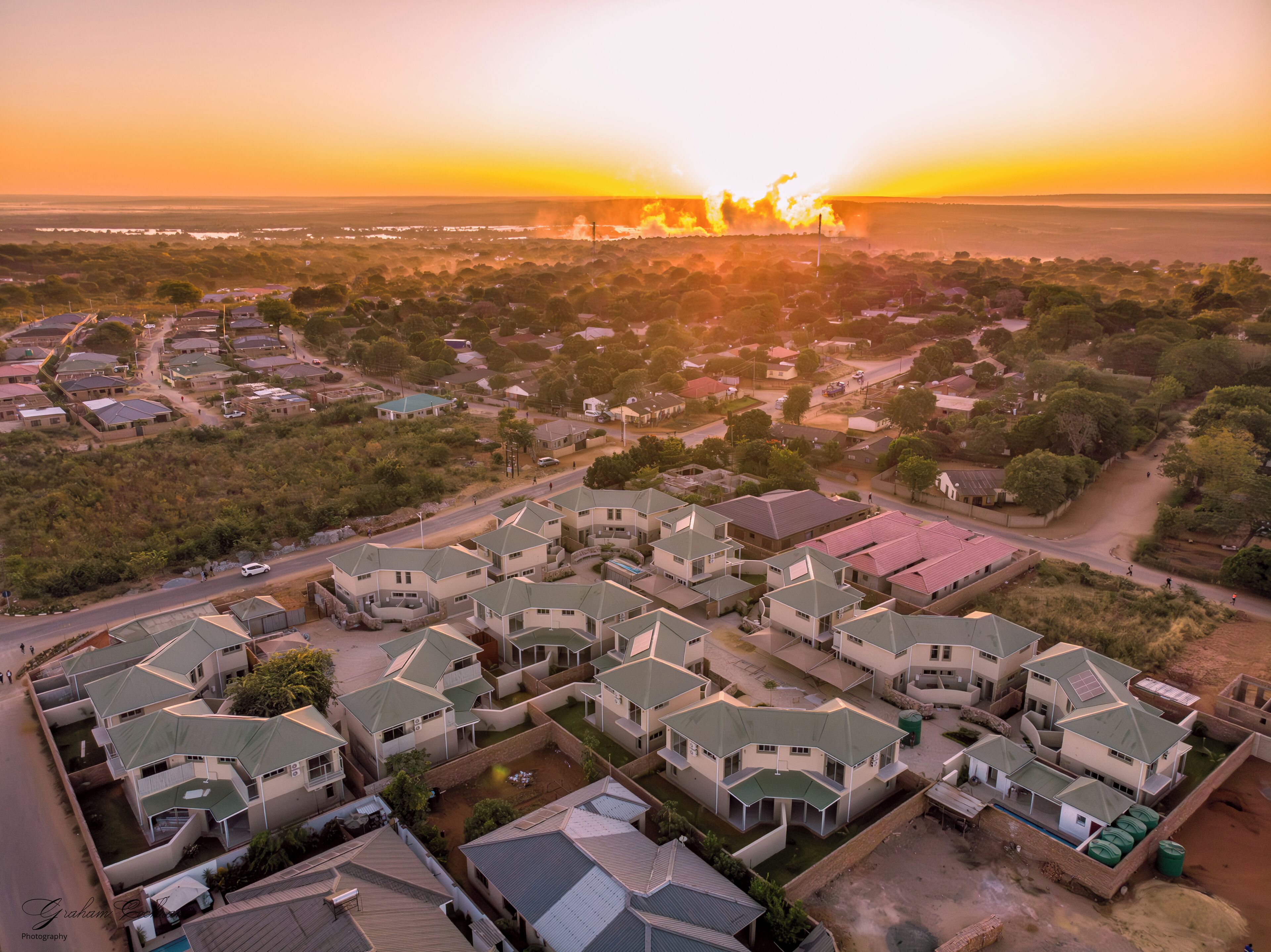 An aerial view of a residential area with houses, roads, and a sunset in the background.