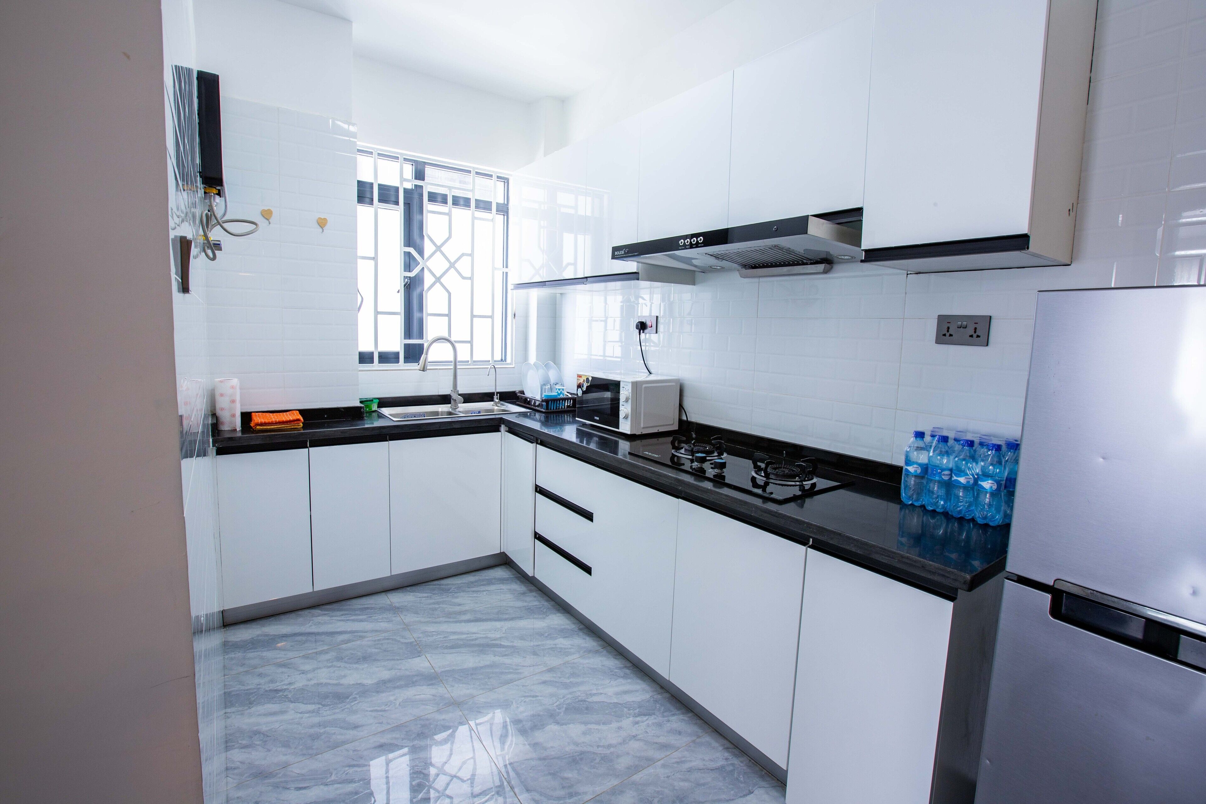 Une cuisine moderne avec des meubles blancs, un plan de travail noir, un réfrigérateur en acier inoxydable et une fenêtre ornée de barreaux décoratifs.