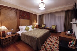 Habitación de hotel con una cama grande, dos mesitas de noche con lámparas, un escritorio con silla, un televisor y una alfombra estampada.