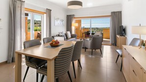 A modern hotel room with a dining area, a sofa set, a TV, and a balcony with a view. - Casa Serenidade - Vale de Ribeira (Arão (Mexilhoeira Grande))
