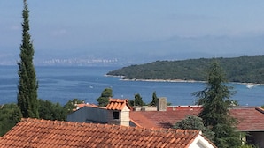 Eine Küstenansicht mit einem Gebäude mit roten Ziegeln, blauem Meer und hügeliger Landschaft im Hintergrund.