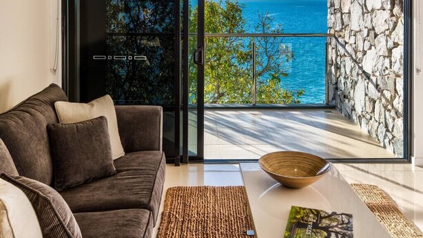A modern living room with a sofa, a coffee table, and a view of the sea through large glass doors. - Edge Apartment 15, Edge Apartment 15 on Hamilton Island (Hamilton Island)