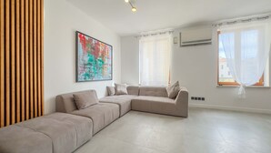 A spacious living room with a large sectional sofa, a colorful abstract painting, and large windows with sheer curtains. - Le Riviera (Cannes)