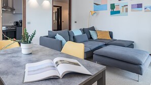 Een moderne woonkamer met een grijze bank, een bijzettafeltje en een plant in pot.