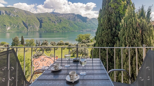 Een balkon met een tafel gedekt voor twee, met uitzicht op een meer en bergen.