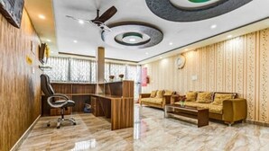 A modern hotel lobby with a wooden reception desk, a comfortable sofa, and a ceiling fan. - iROOMZ Suchira Lodge (Mandya)