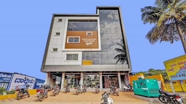 A multi-story building with a modern design, featuring a ground-level shop and several parked motorcycles. - iROOMZ Suchira Lodge (Mandya)