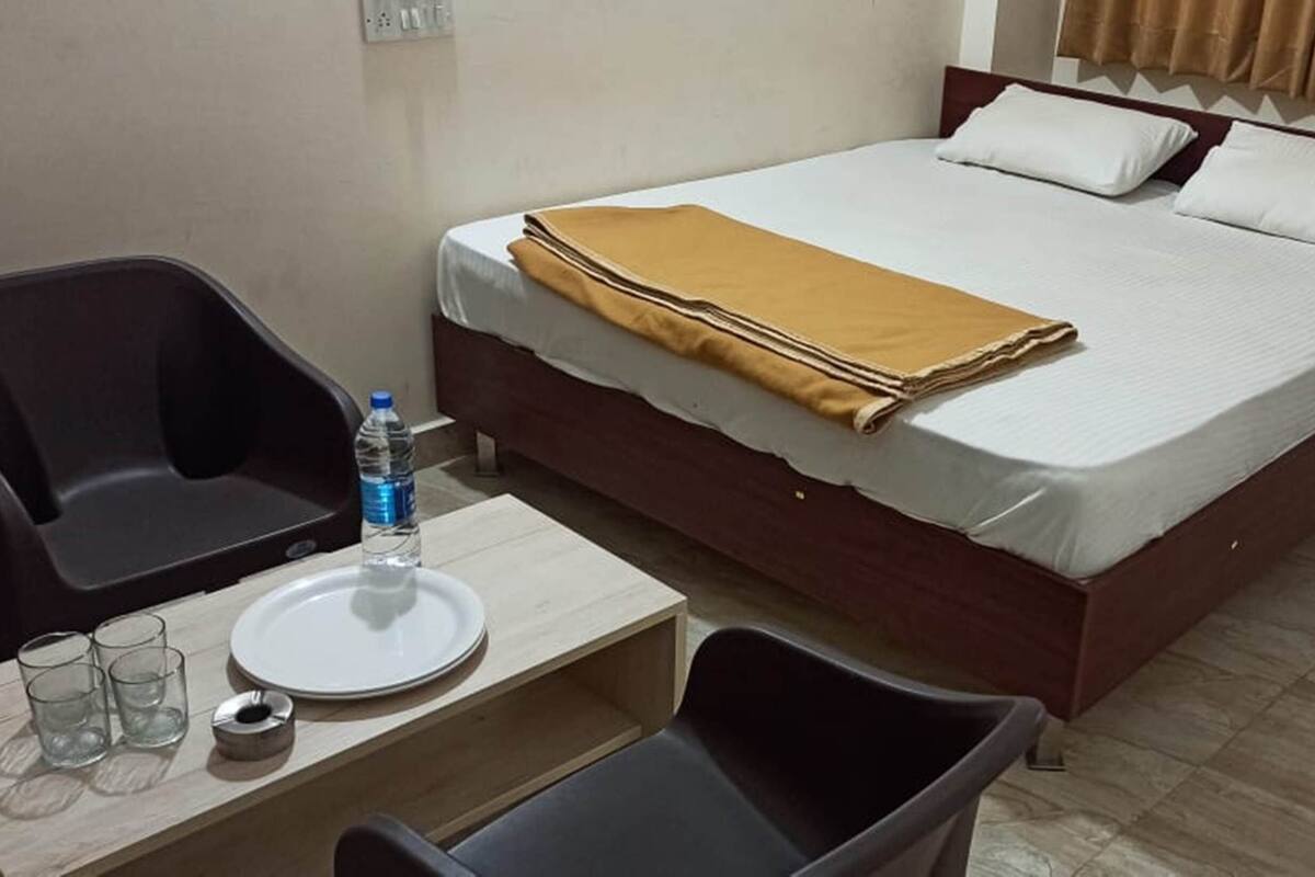 Quarto de hotel com uma cama, uma pequena mesa com um prato, copos e uma garrafa de água.