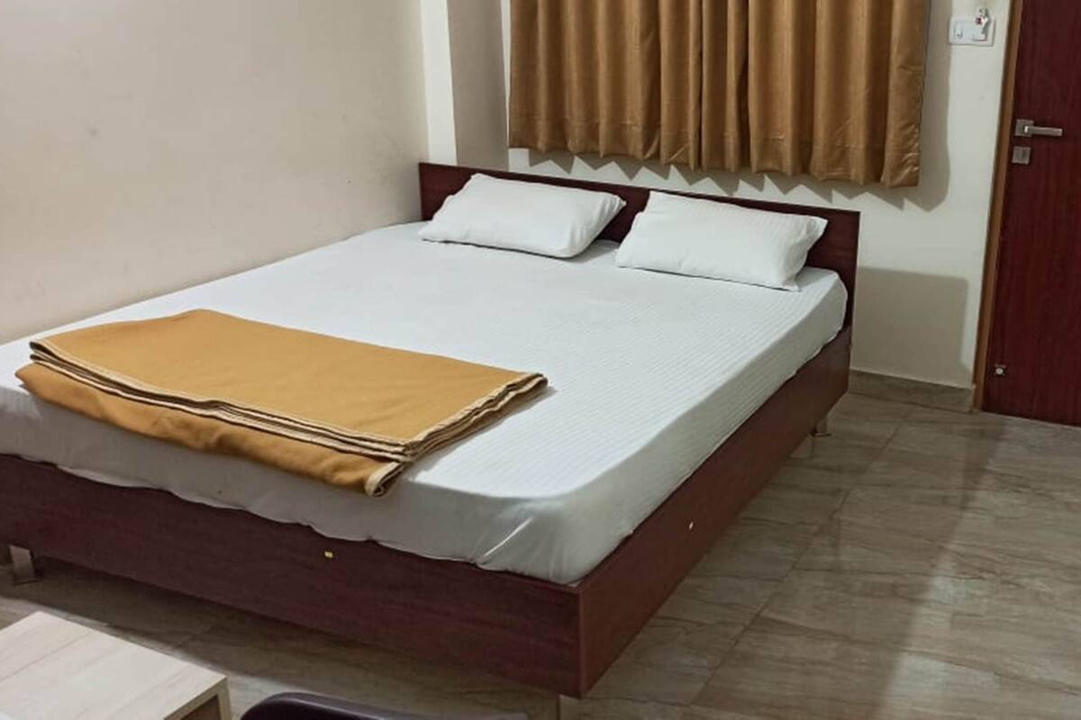 Cama bem arrumada com manta marrom, cabeceira de madeira e roupa de cama branca.