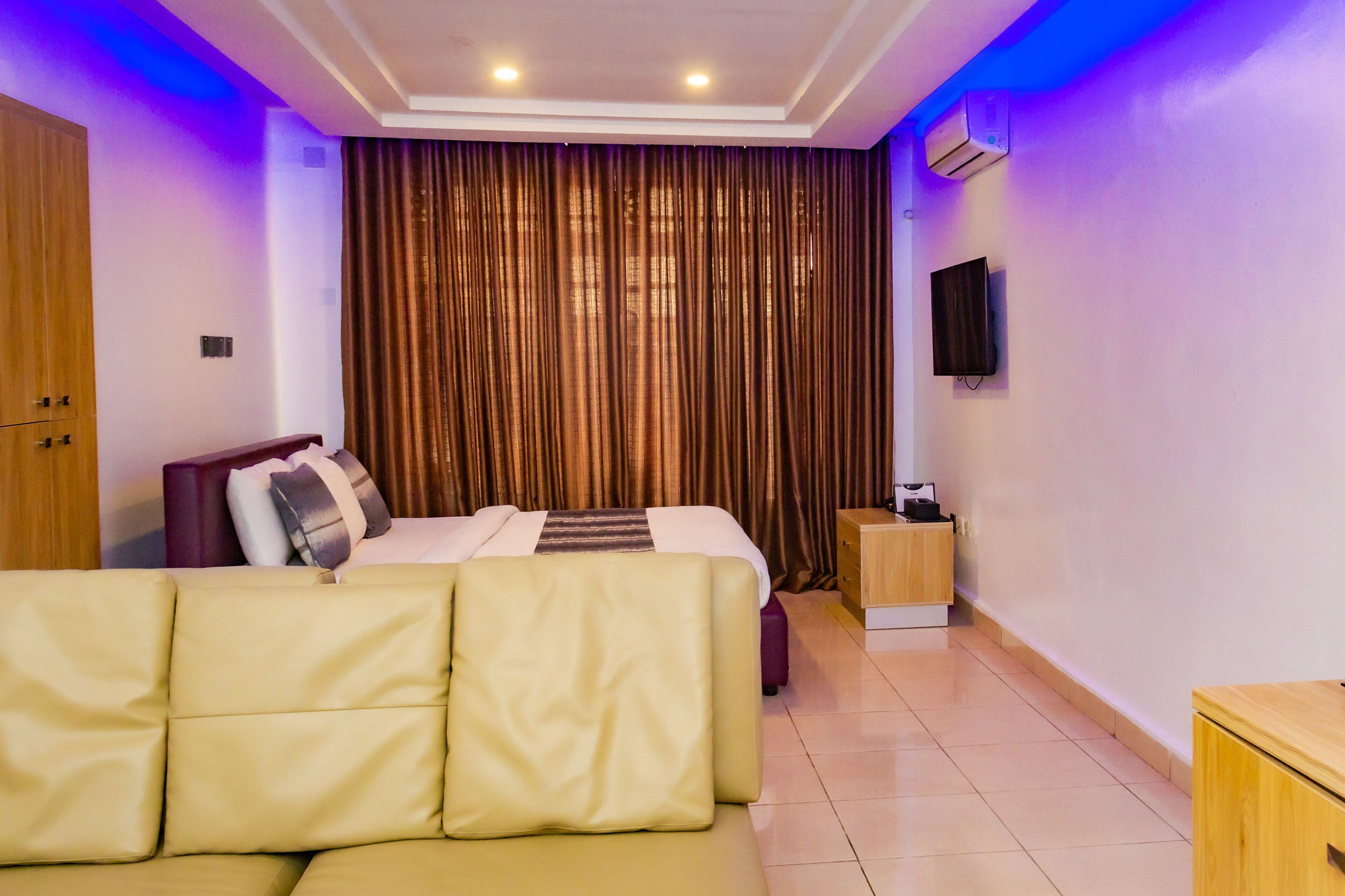 A hotel room with a bed, a sofa, a TV, and a small wooden side table.