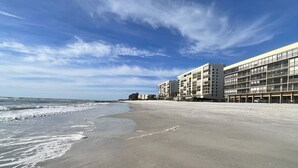 A beach with a row of multi-story buildings, a clear sky, and waves approaching the shore. - NEW! Luxuriously Updated & Renovated Beachfront Retreat- Walkable to Fun!! (Madeira Beach)