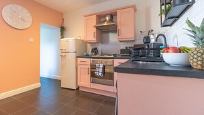 A modern kitchen with pink cabinets, a stainless steel range hood, and a large clock on the wall. - Afton (Lancaster)