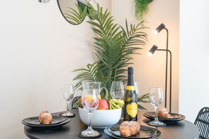Una mesa de comedor dispuesta con un bol de fruta, una botella de champán y pasteles.