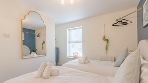 A bedroom with two beds, a large mirror, a window with blinds, and a hanging plant. - Afton (Lancaster)