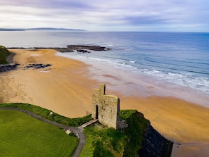 A coastal landscape with a stone structure on a grassy cliff overlooking a sandy beach and the sea. - Ballybunion Holiday Cottages (Ballybunion)