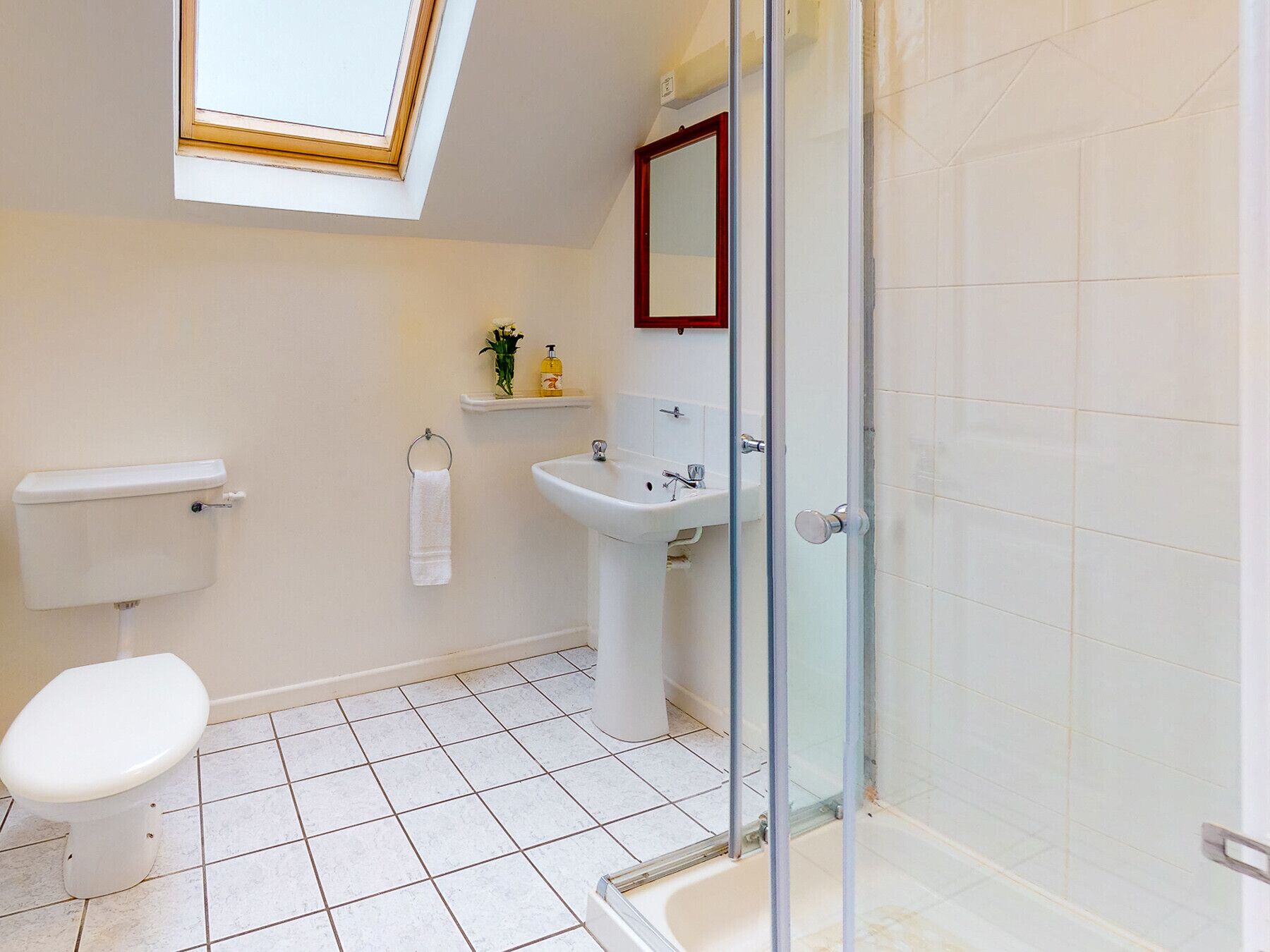 A bathroom with a skylight, toilet, sink, and shower.