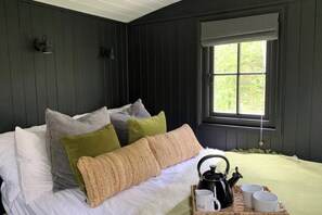 A bedroom with a bed, pillows, a window, and a tray with a kettle and mugs.