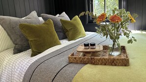 Une chambre moderne avec une tête de lit en bois foncé, une couvre-lit à rayures et une table de chevet ornée d’un vase de fleurs et de deux pots.