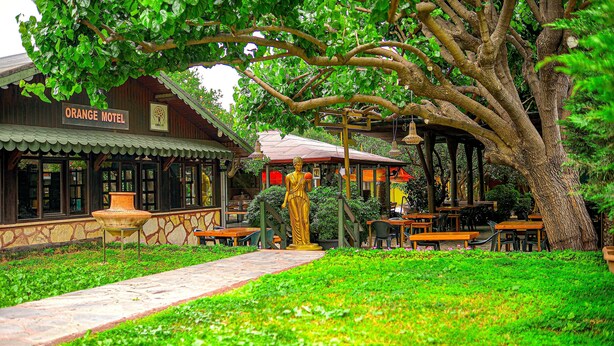 A building labeled 'Orange Motel' with outdoor seating and a statue. - Çıralı Orange Motel (Kemer)