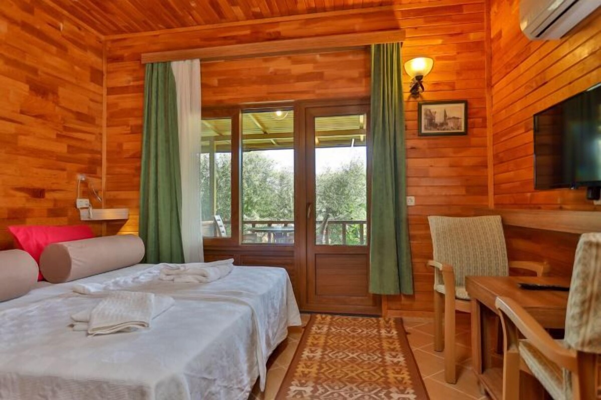 A wooden cabin room with a bed, a table, a chair, and a TV.
