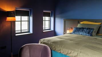 A bedroom with a bed, two windows, a floor lamp, and a chair.