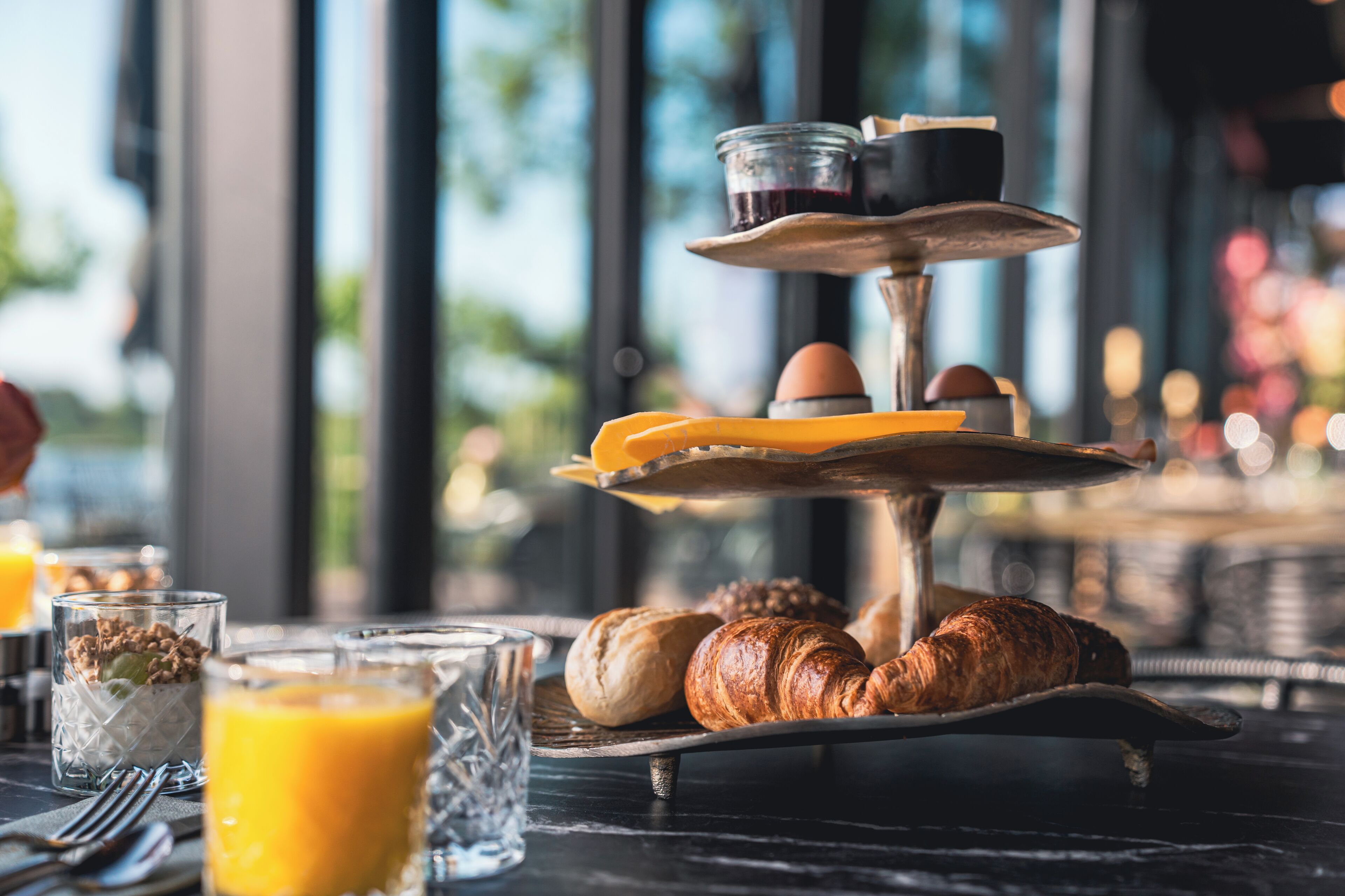 A breakfast setup with croissants, orange juice, and a tiered serving tray with eggs and coffee.