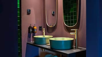 Une salle de bain au design moderne, dotée d’un grand miroir, d’un lavabo rond et d’une étagère où sont rangées les serviettes.