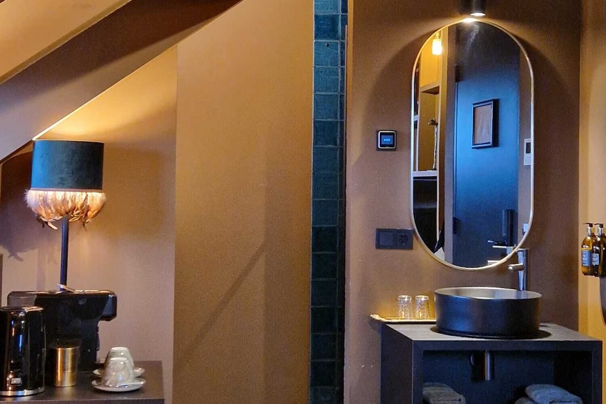 A modern bathroom with a large mirror, a sink, and a towel rack. There is a coffee machine and a towel dispenser on the counter.