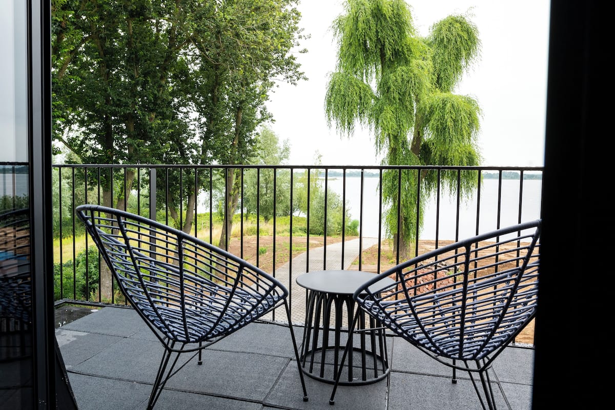 A balcony with two metal chairs and a small table, overlooking a body of water and trees.