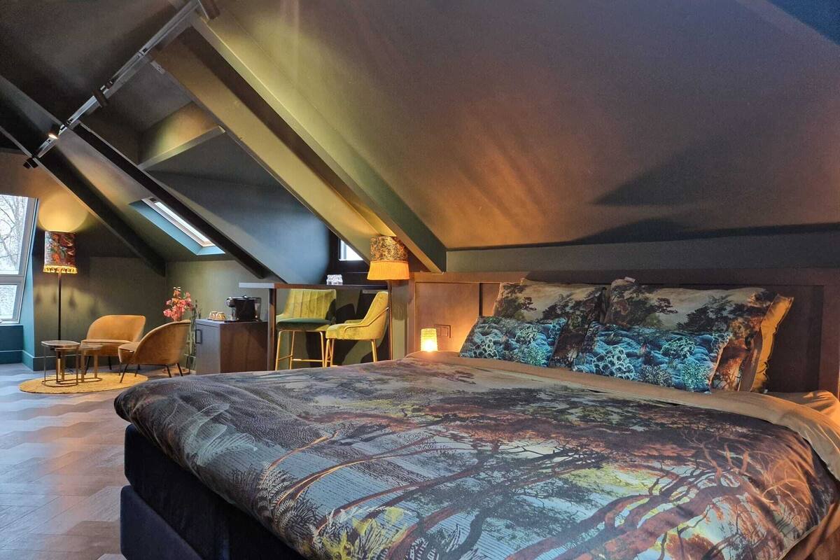 A modern bedroom with a large bed, a desk, and two chairs.