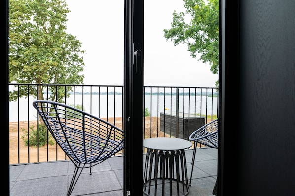 A balcony with two chairs and a table, overlooking a body of water and trees. - Boutique Hotel de Bungelaer (Beers)