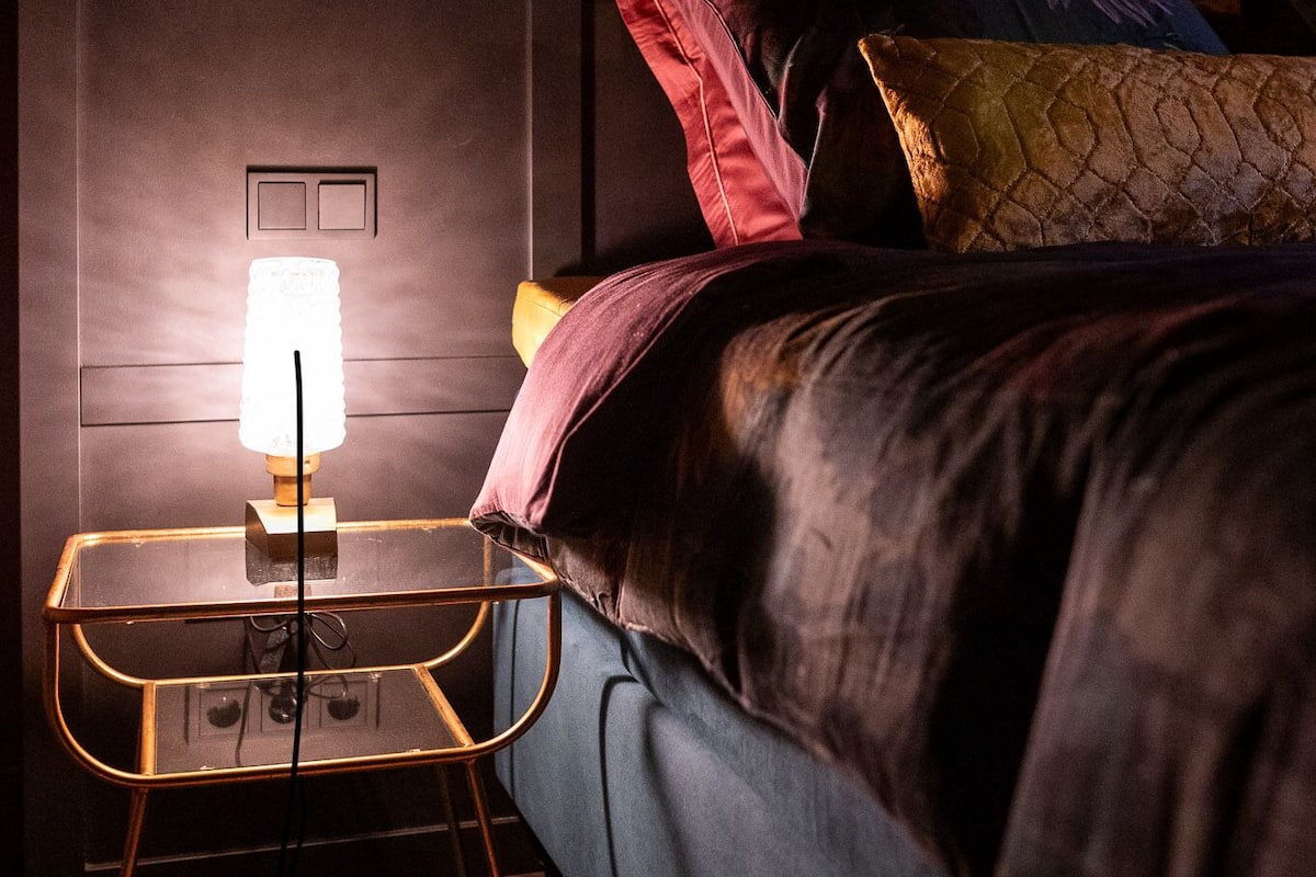 A bedroom with a bed, a bedside table with a lamp, and a wall switch.
