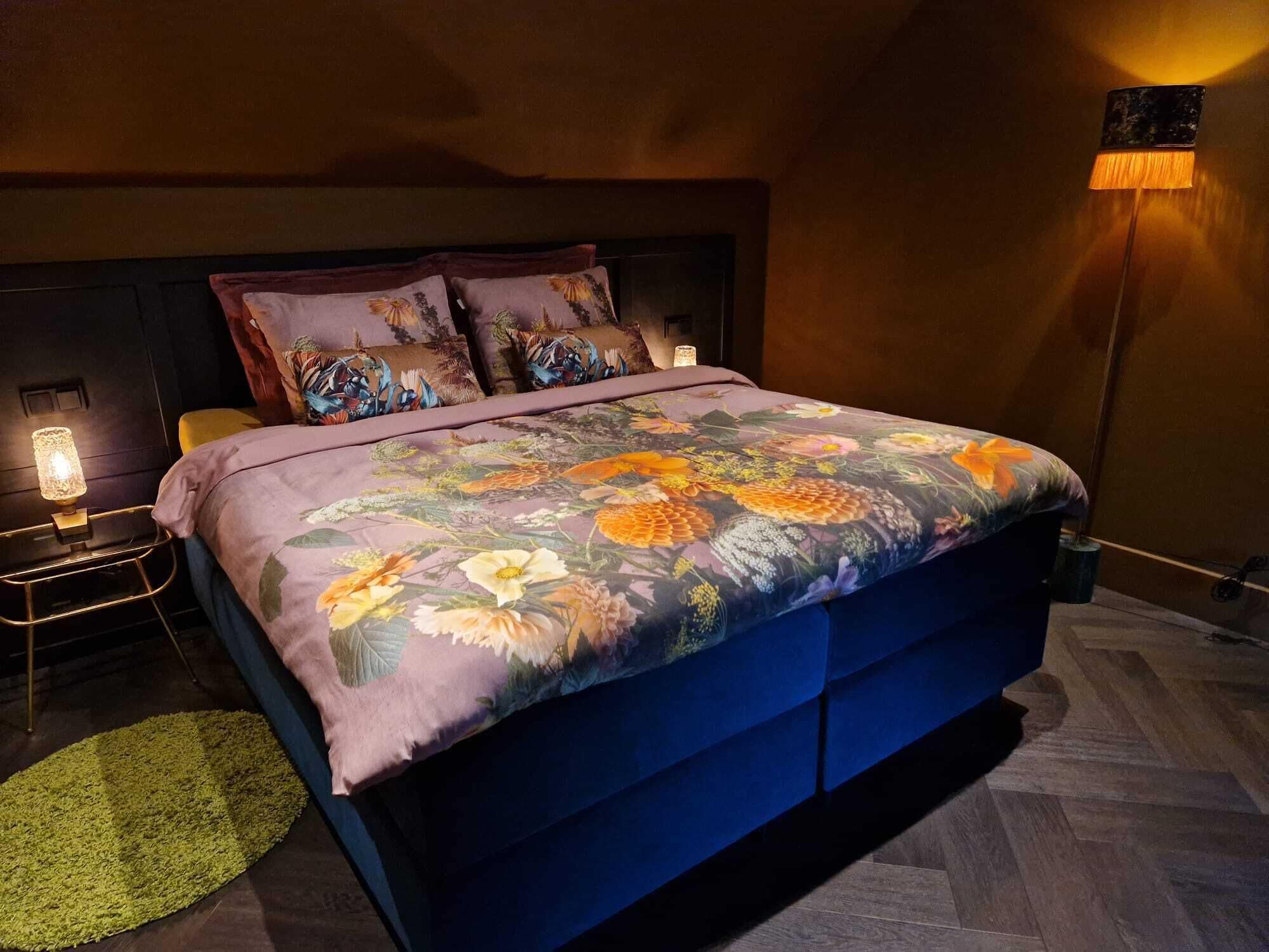 Een slaapkamer met een groot bed, een nachtkastje met een lamp en een vloerlamp.