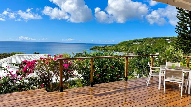 Eine Holzterrasse mit Blick auf das Meer und einen üppigen Garten mit rosa Blüten.