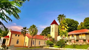 Eine Kirche mit rotem Dach und einem Glockenturm, umgeben von Palmen und blauem Himmel.
