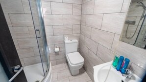 A modern bathroom with a glass shower enclosure, a toilet, and a sink with toiletries. - Studio Close to Selly Oak Train Station (Birmingham)