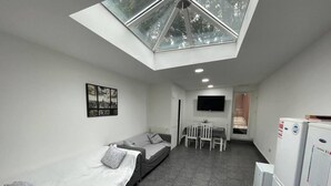 A compact room with a skylight, a bed, a small table with chairs, a TV, and a refrigerator. - Studio Close to Selly Oak Train Station (Birmingham)