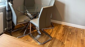 A modern room with a glass table and chairs, a mounted TV, and a window with curtains. - Inverness Highland Apartment (Inverness)