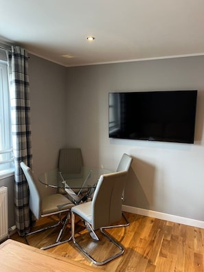 Enjoy a compact living space with a glass-top dining table and flat-screen TV, perfect for relaxation and entertainment.