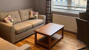 A living room with a sofa, a wooden coffee table, and a chair. - Inverness Highland Apartment (Inverness)
