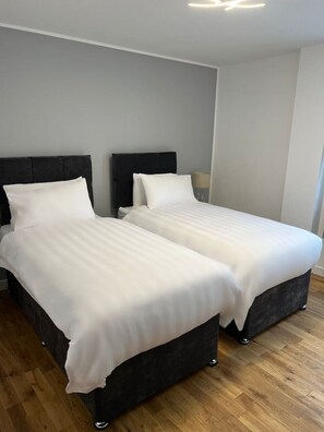 Two single beds with dark headboards and white bedding, set in a simple, clean room with a wooden floor.
