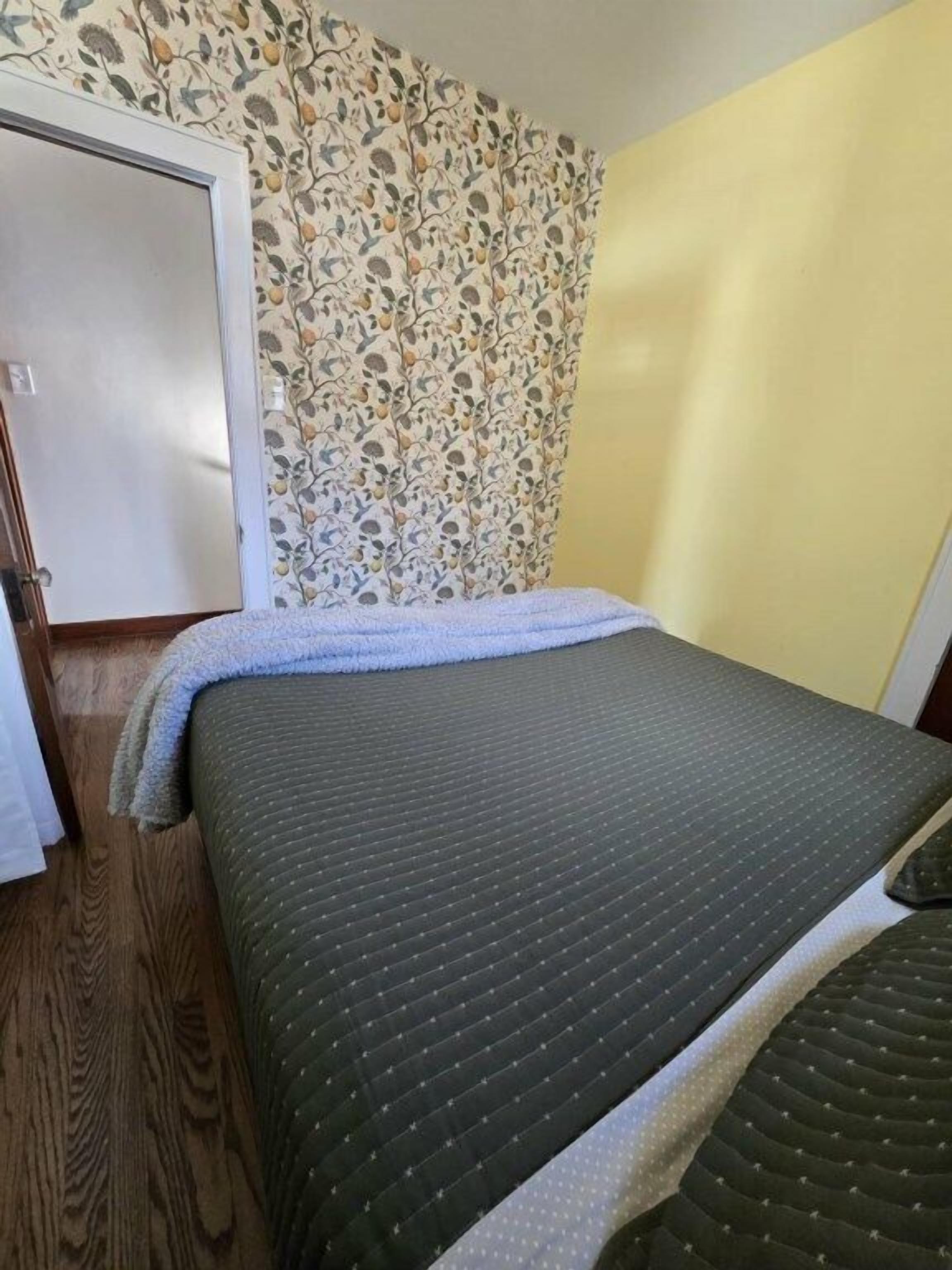 A room with a bed, a door, and a patterned wallpaper.