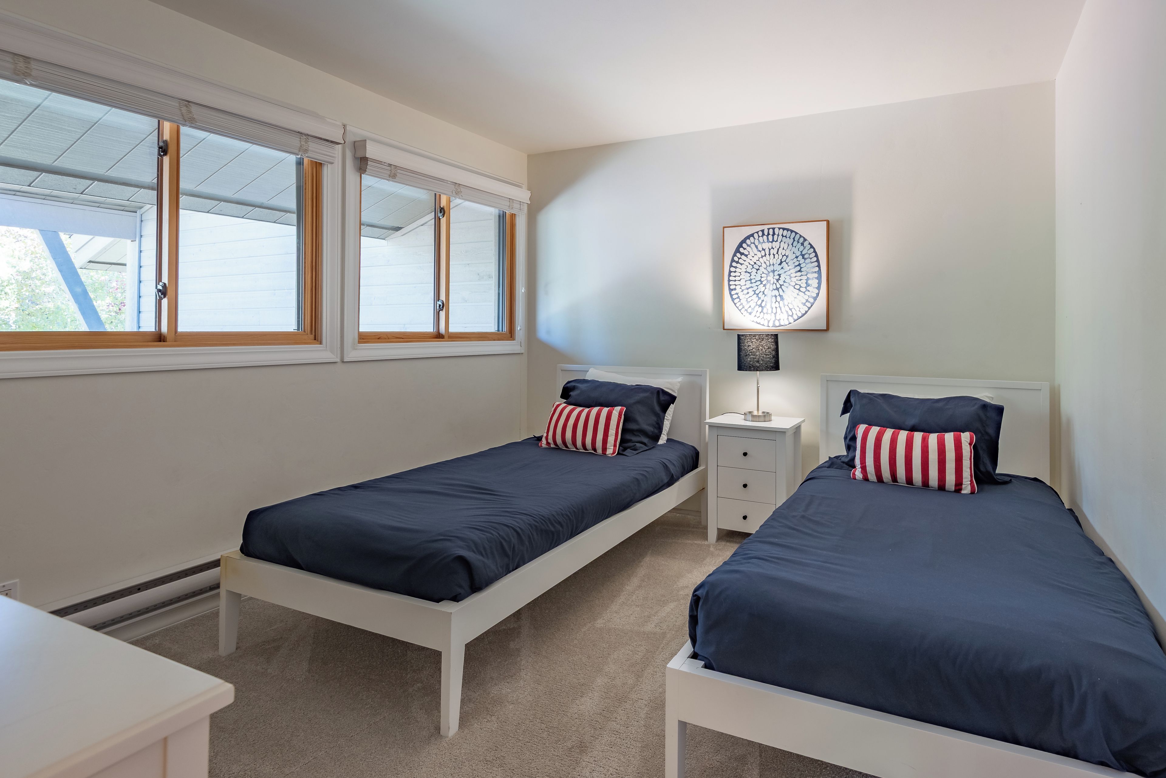 A bedroom with two single beds, a nightstand, a lamp, and a window with blinds.