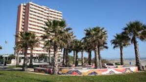 A multi-story hotel with a flat roof and balconies, surrounded by palm trees and a landscaped area with a colorful mural. - Seafront Apartment for Rent 6 Sleeps Skyscraper (Fermo)