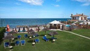 A coastal property with a grassy lawn, blue lounge chairs, and a view of the sea. - Seafront Apartment for Rent 6 Sleeps Skyscraper (Fermo)