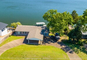 An aerial view of a lakeside property with a house, a covered patio, and a boat dock.