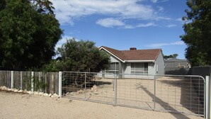Une propriété clôturée comprenant une maison, un sol en gravier et des arbres.
